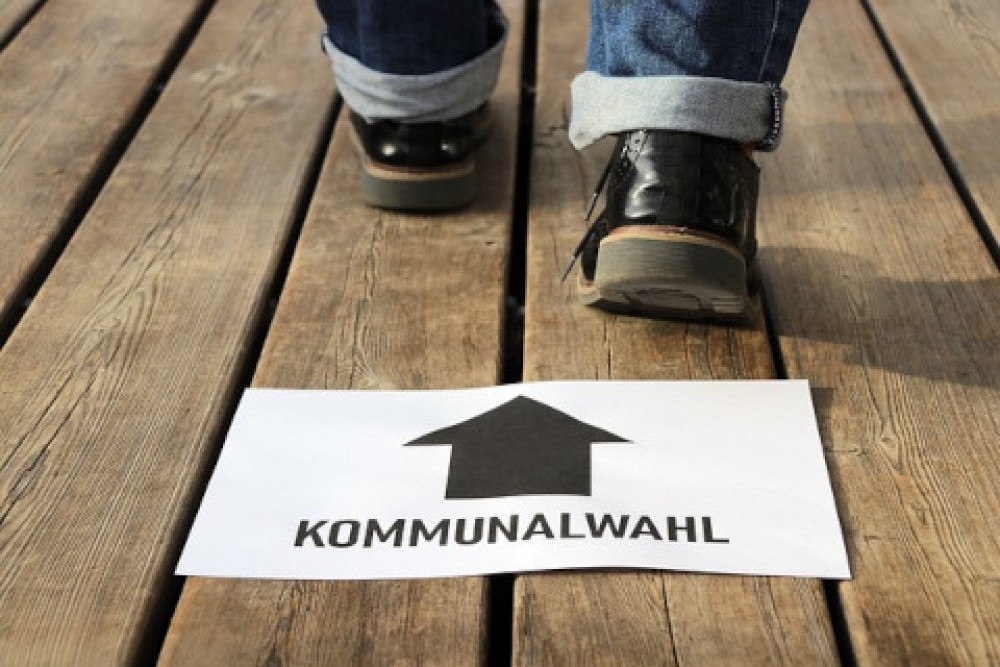 Schild mit Aufschrift &quotKommunalwahlen&quot vor zwei sich nach vorn bewegenden Füßen
