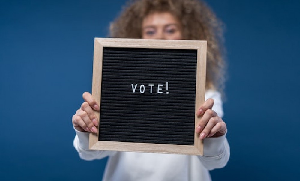 Eine Frau hält eine Tafel mit dem Slogan &quotVote!&quot in die Kamera. Foto: cottonbro studio via pexels.com