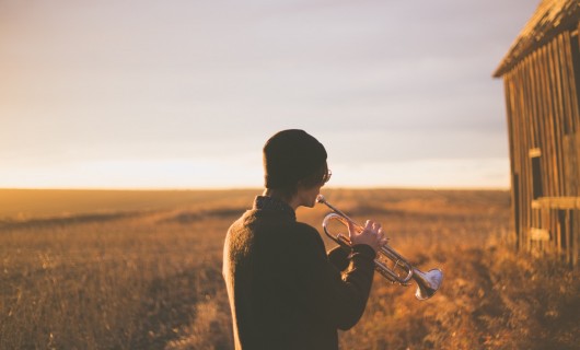 Ein junger Mann steht auf einem Feld und spielt Trompete.